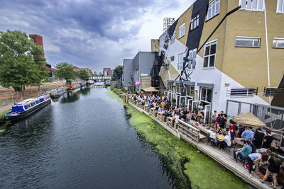 People on river amidst buildings in city against sky