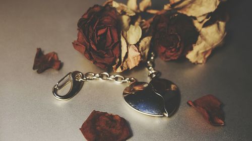 Close-up of heart shape locket and wilted flowers on floor