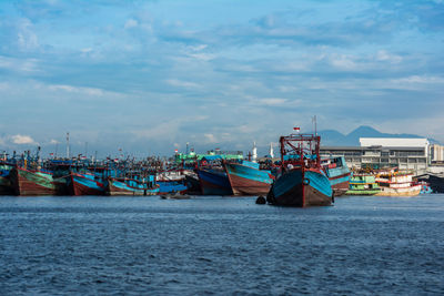 Fishing boats moored at harbor against sky