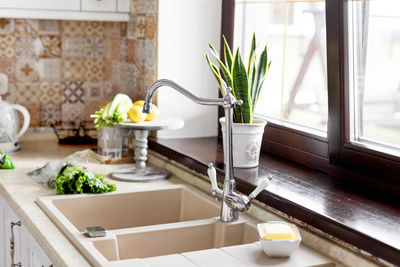 The vegetables are on the table next to the sink. kitchen faucet, sink, kitchen, vegetables.