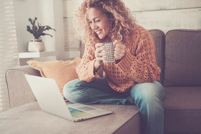 Young woman using phone while sitting on sofa at home