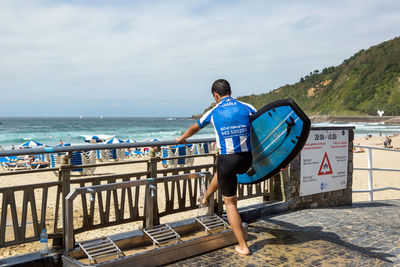 Rear view full length of surfer washing leg at beach