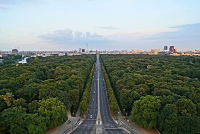 Street amidst trees leading towards city against sky