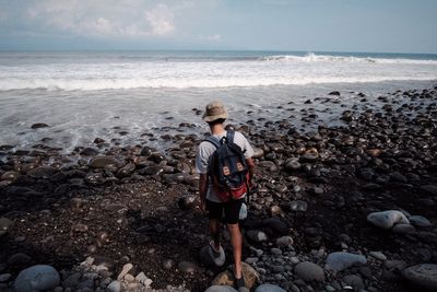 Full length rear view of traveler walking at beach against sky