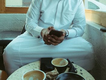 Midsection of man using mobile phone while sitting on table