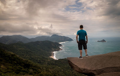 Full length rear view of man standing on landscape against cloudy sky