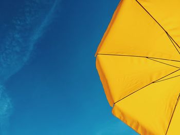 Low angle view of yellow parasol against blue sky