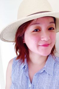 Portrait of young woman wearing hat against white wall