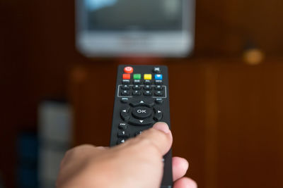 Cropped hand of person holding remote control while watching tv