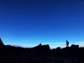 Silhouette man standing on rock against clear blue sky