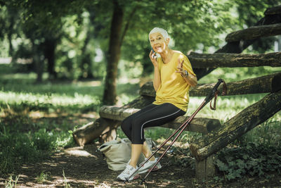 Active senior woman taking a workout break, talking over the phone after nordic walk exercise