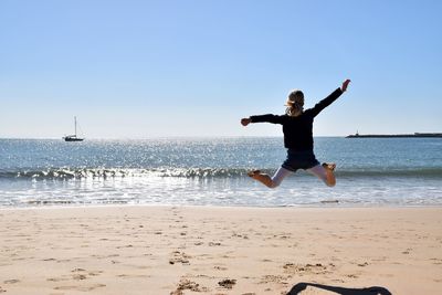 Full length of woman jumping on beach against clear sky
