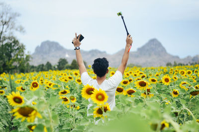 Rear view of man with arms raised on sunflower field