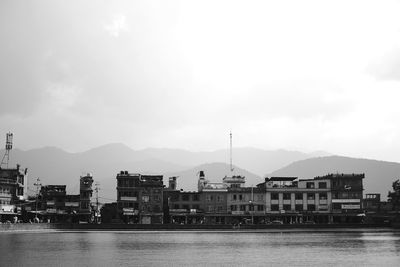 Buildings at waterfront against cloudy sky