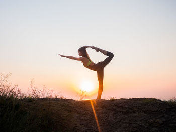 Side view of woman doing natarajasana on field against sky during sunset