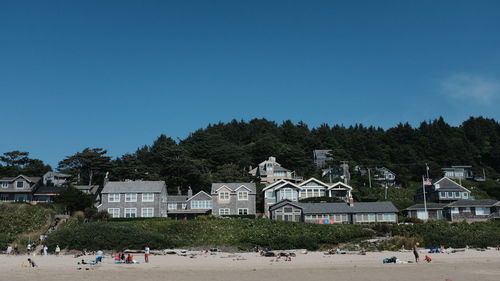 Beach houses line the shore with evergreen trees covering a hillside behind