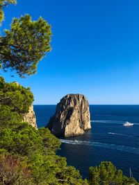 Scenic view of rock formation in sea against clear blue sky