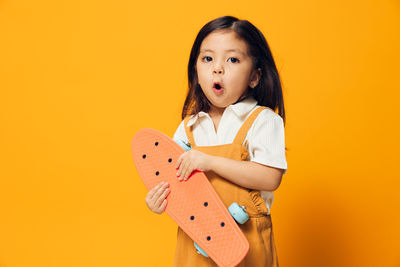 Portrait of cute baby girl holding toy against yellow background