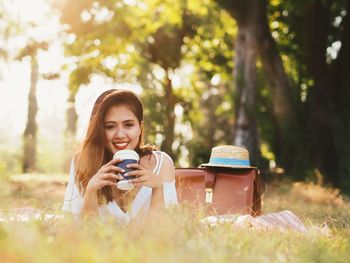 Portrait of young woman having coffee while resting on field
