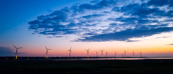 Silhouette wind turbines at beach against sky during sunset