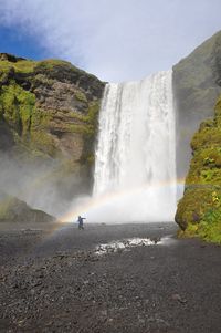 Man with arms outstretched standing by waterfall