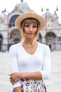 Portrait of woman wearing hat standing against city in background