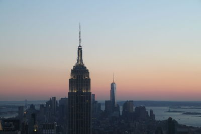 Empire state building in city against sky during sunset