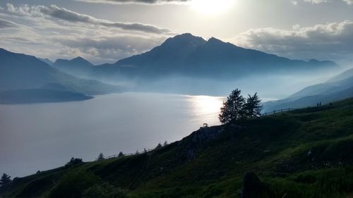 Scenic view of lake and mountains against sky during foggy weather