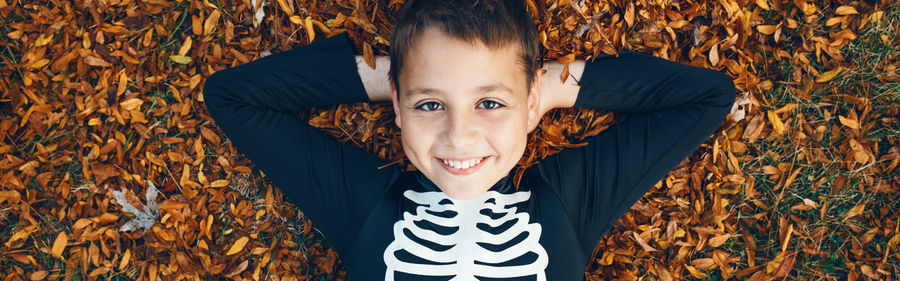 Portrait of cute boy lying down on autumn leaves