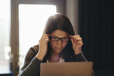 Mature businesswoman wearing eyeglasses while looking at laptop in office