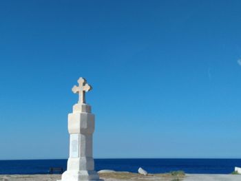 Statue by sea against clear blue sky