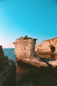 Rock formations on shore against clear blue sky