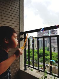 Side view of boy blowing bubbles in balcony