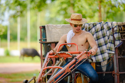 Shirtless man riding agricultural machinery at farm