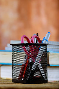 Close-up of pens and scissor in desk organizer on table against wall