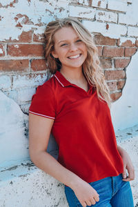 Portrait of smiling young woman standing against brick wall