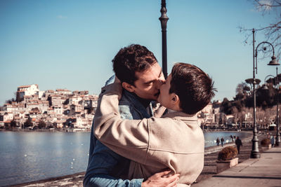 A young couple kisses while taking a photo on the shore of lake bracciano. 