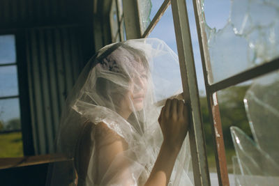 Thoughtful woman covered with fabric by window