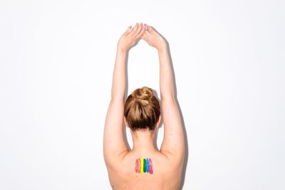 Rear view of shirtless woman with colorful paints on her back by white wall