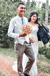 Portrait of married couple holding bouquet walking outdoors