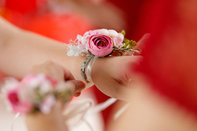 Close-up of woman putting pink flower bracelet on hand