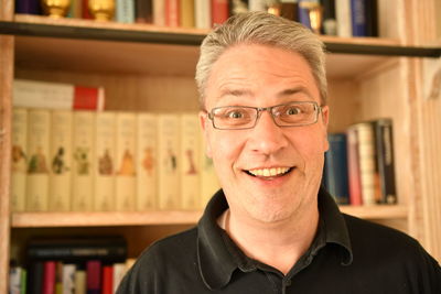 Close-up portrait of man smiling against bookshelf in library