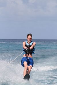 Young man wakeboarding in sea against sky