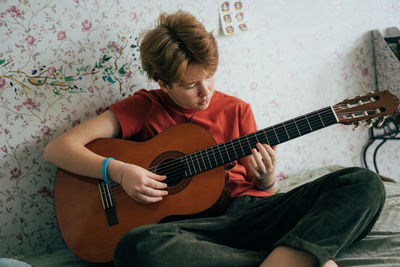 Romantic adolescent redhead girl learning to play the guitar while sitting in the room.