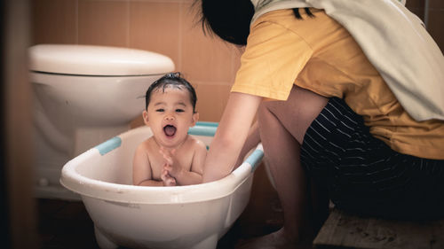 Midsection of mother bathing baby daughter in bathroom