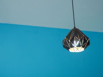 Low angle view of illuminated pendant light against blue sky