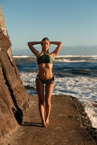Beautiful young woman wearing bikini by rock formation at beach