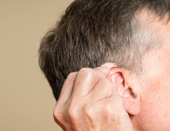 Close-up of senior man holding hearing aid against beige background