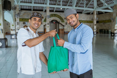 Portrait of smiling men holding carry bag standing at mosque