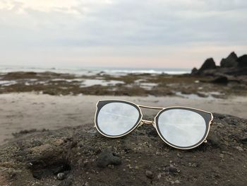 Close-up of eyeglasses on sand at beach against sky